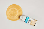 Load image into Gallery viewer, Bottle of Pale Gold Polyvine Metallic Paint being poured onto a pale grey surface
