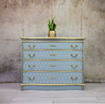 Load image into Gallery viewer, Sunlit Diamonds Redesign with Prima Stencil from the Kacha Collection - art deco fan design stencilled in white on a pale blue and gold chest of drawers
