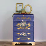 Load image into Gallery viewer, Les Roses Redesign with Prima Transfer from the Kacha Collection featuring gold french script and delicate pink roses applied to a vibrant cobalt blue chest of drawers with gold leaf feet
